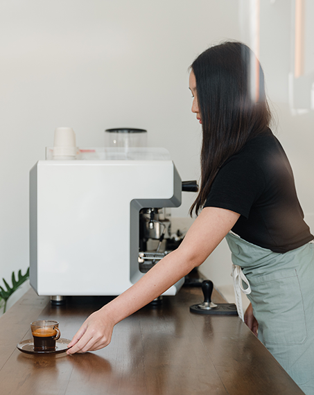 En kvinnlig barista serverar kaffe på cafébänken.