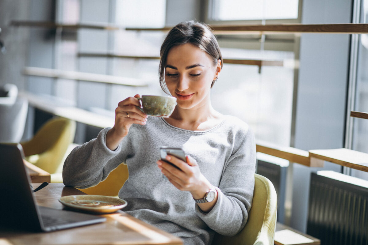Kvinna som sitter på ett café och dricker kaffe och arbetar på en dator.